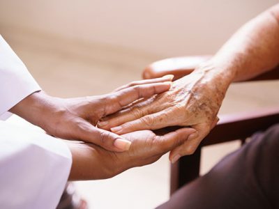 Old people in geriatric hospice: Aged patient receives the visit of a female black doctor. They shake their hands and talk in the hospital.