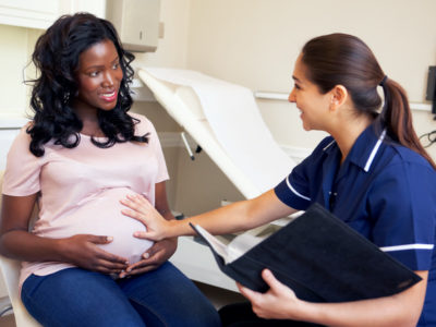 Pregnant Woman Smiling Being Given Ante Natal Check By Nurse