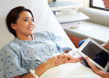 Happy Smiling Nurse Talking To Female Patient On Ward Using Digital Tablet